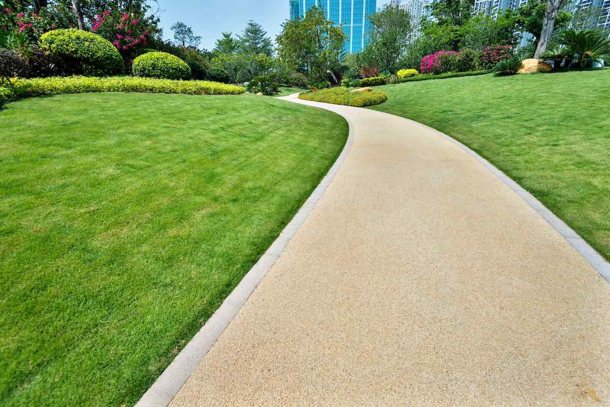 Commercial landscaping and turf maintenance, with a walking path and business building in the background.